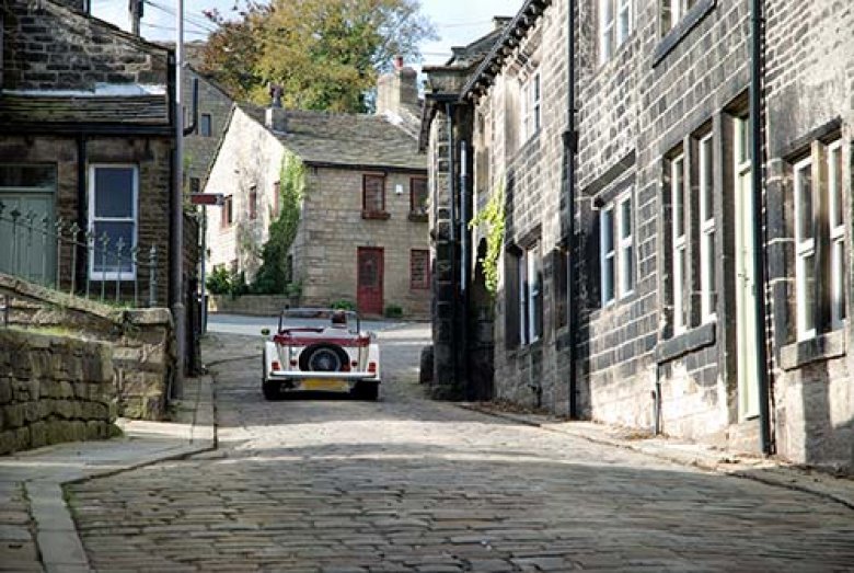 Old classic car sriving up hill through cobbled streets.